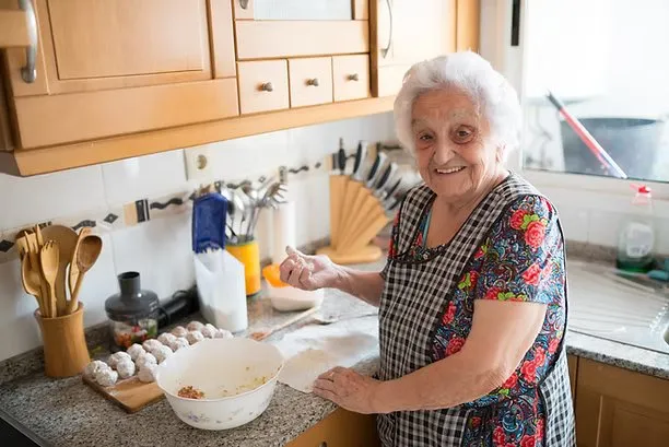 Idosa sorrindo enquanto cozinha na cozinha de casa