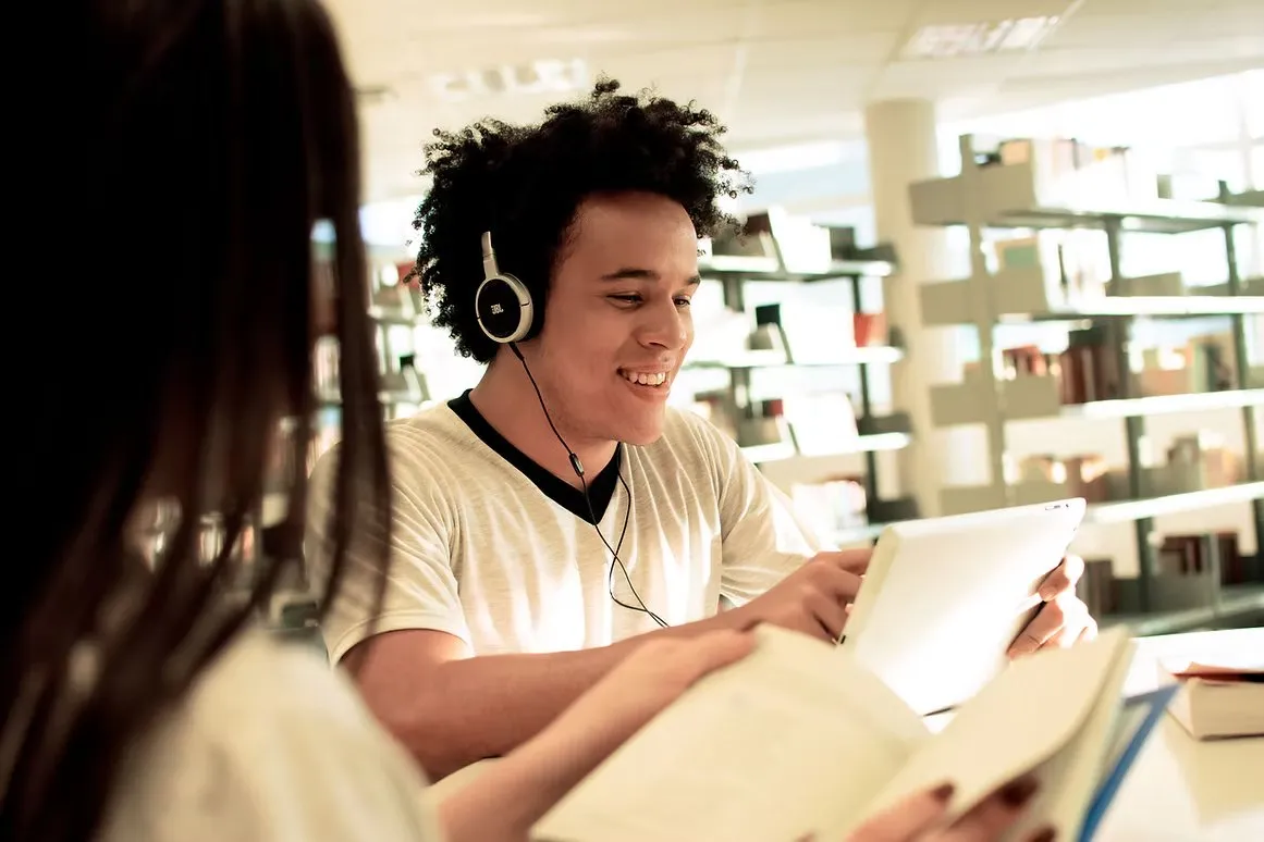 Jovem com fones de ouvido lendo na biblioteca